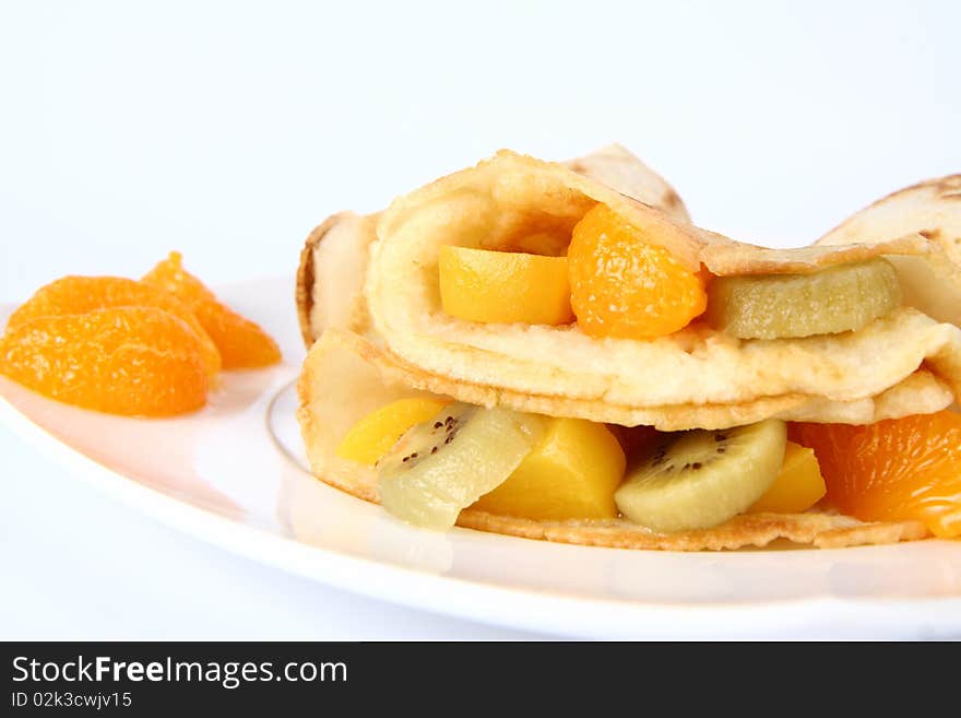 Pancakes stuffed with fruit (peach, kiwi, mandarin) on a plate decorated with fruit in close up