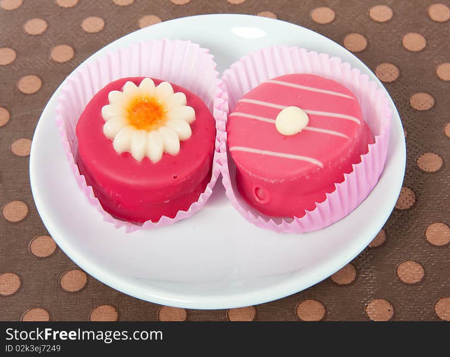 Two pink petit fours on a brown napkin full screen. Two pink petit fours on a brown napkin full screen