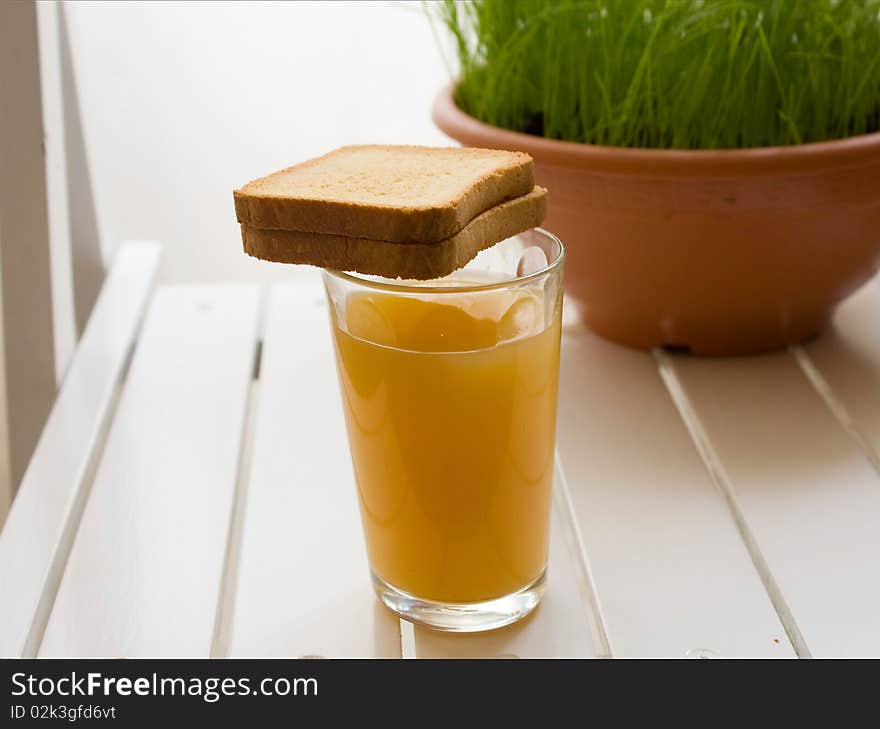 Glass of orange juice with toasts on a white board