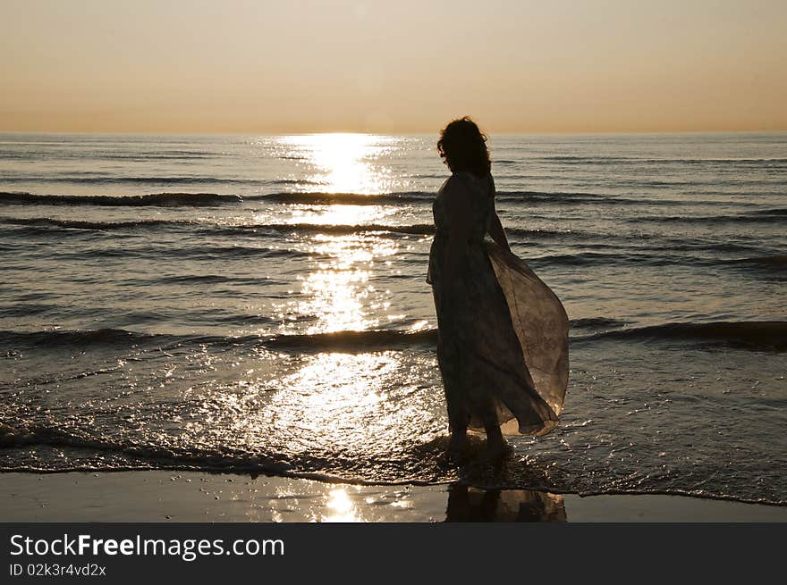 A happy woman standing on the beachin a loose dress, enjoying the beautiful sunset. A happy woman standing on the beachin a loose dress, enjoying the beautiful sunset.