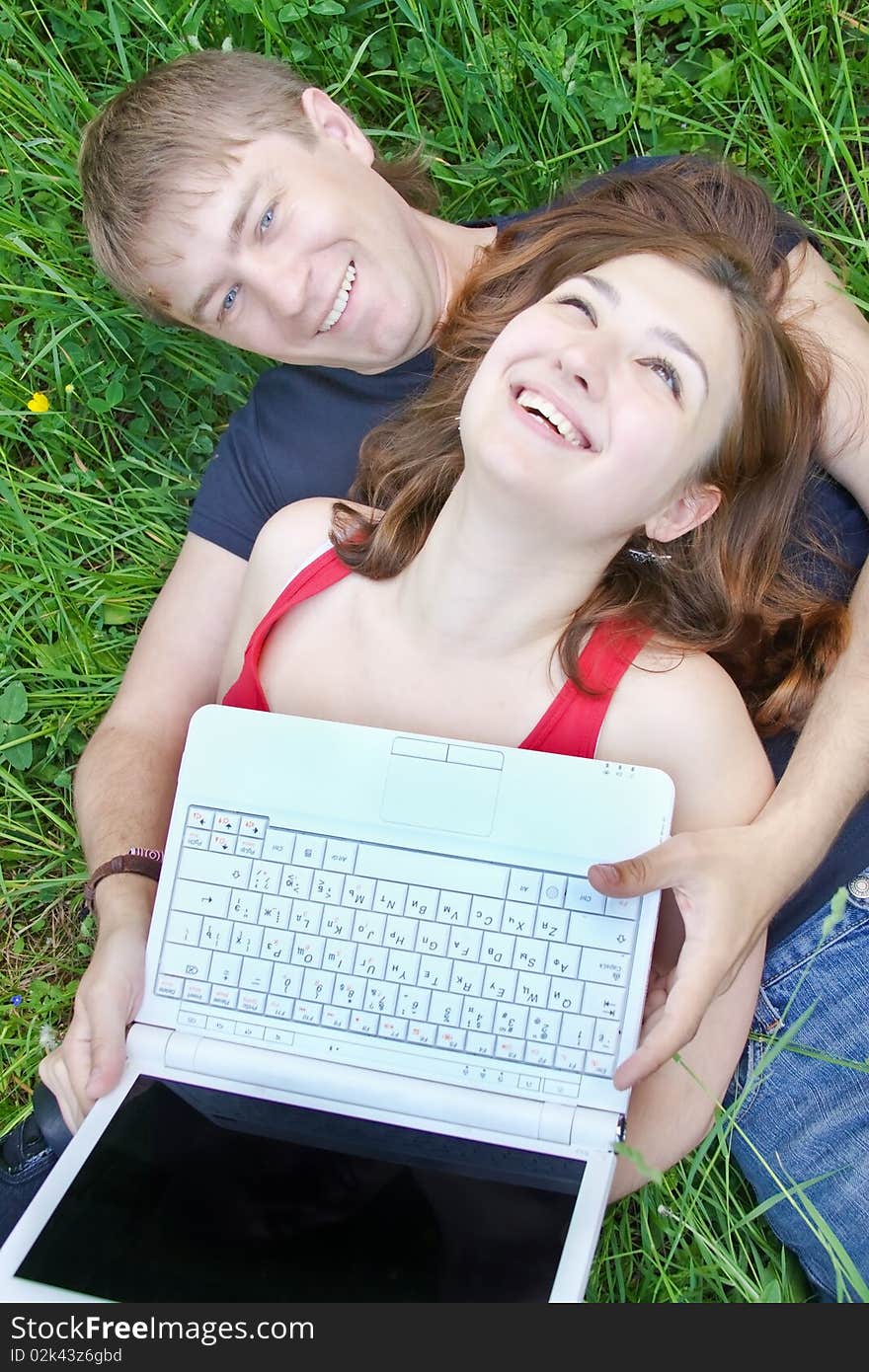 Young pair, on nature with a laptop, lyings on a grass