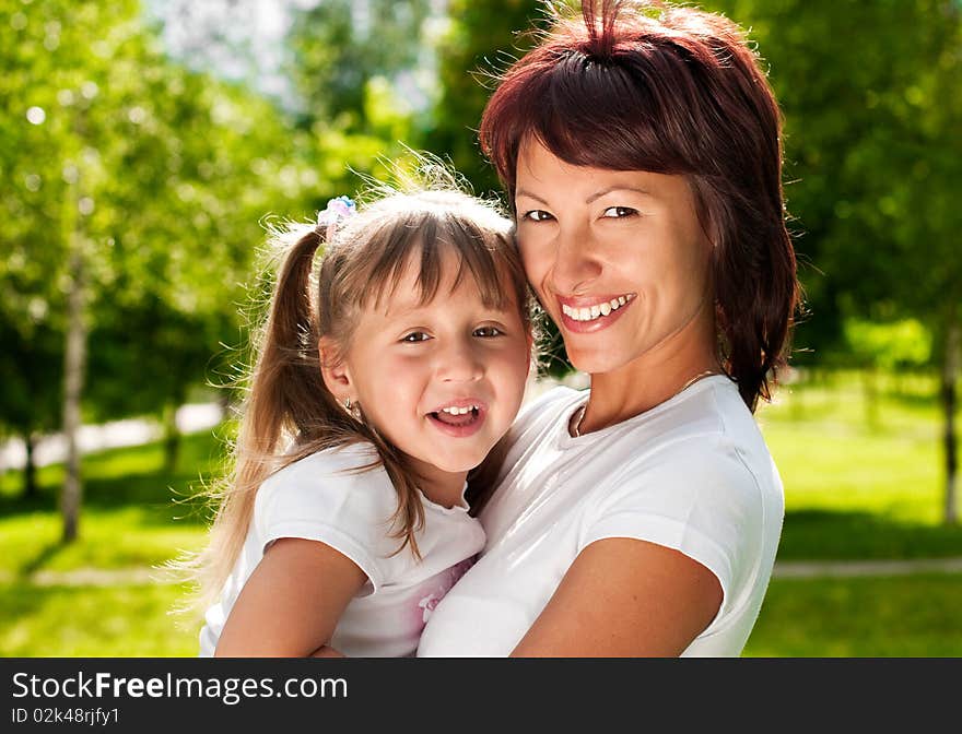 Happy young mother in park with her beautiful small daughter, both smiling and looking in camera. Happy young mother in park with her beautiful small daughter, both smiling and looking in camera