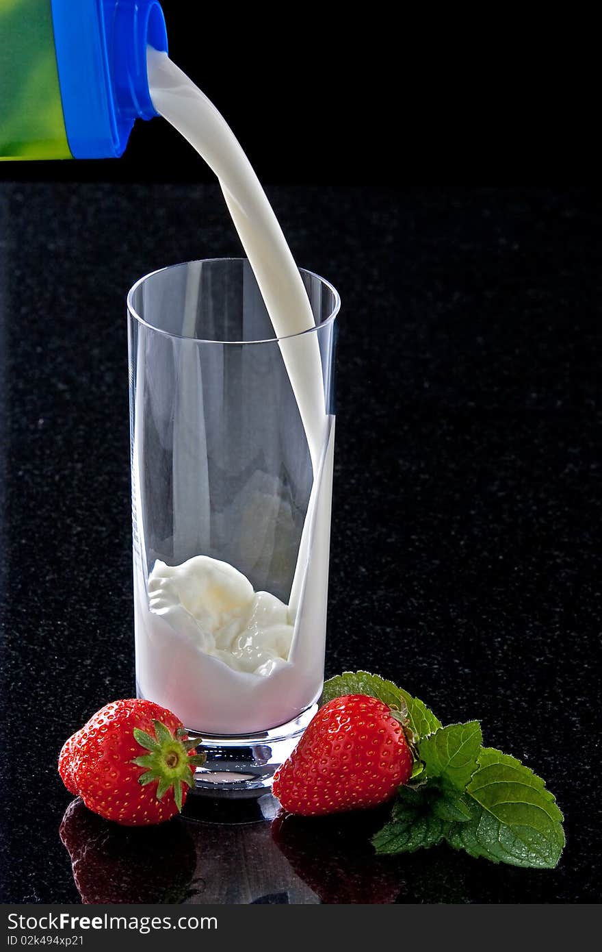 Milk pouring in glass with strawberries and mint leaves. Milk pouring in glass with strawberries and mint leaves