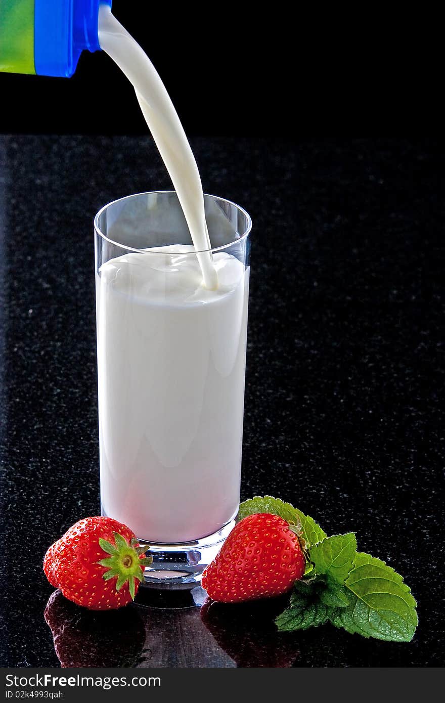 Milk pouring in glass with strawberries and mint leaves. Milk pouring in glass with strawberries and mint leaves