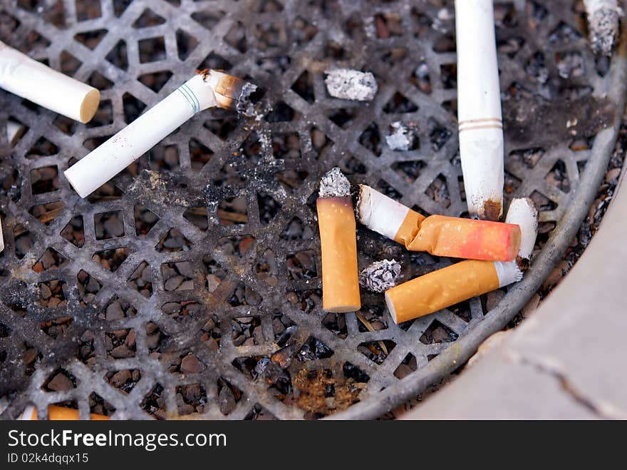 A dirty ashtray with smoked cigarette filters and butts with lipstick on them. A dirty ashtray with smoked cigarette filters and butts with lipstick on them