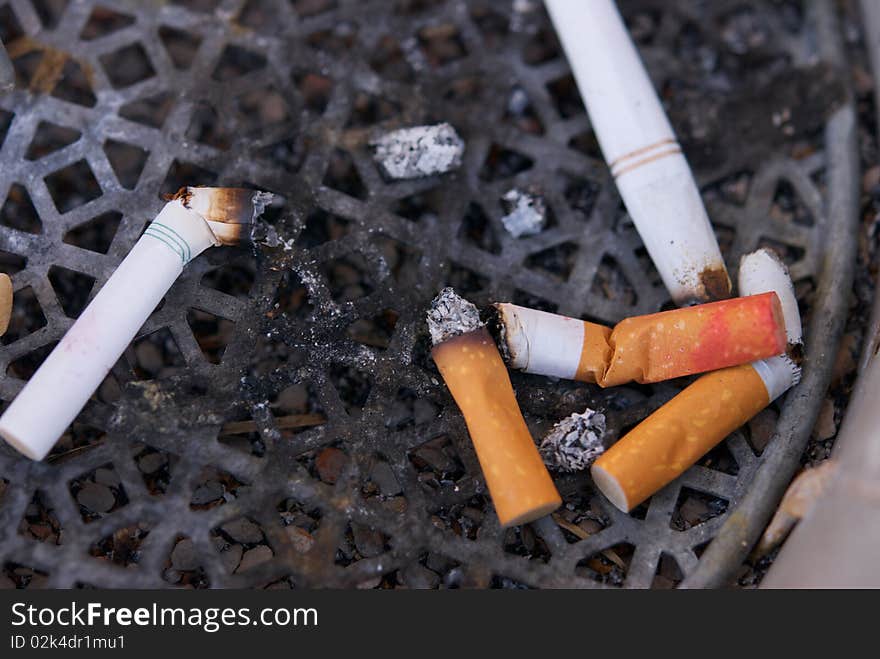 A dirty ashtray with smoked cigarette filters and butts with lipstick on them. A dirty ashtray with smoked cigarette filters and butts with lipstick on them