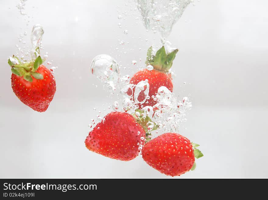 Five strawberries falling in water.