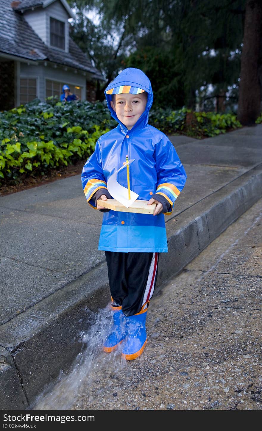 Young boy playing with toy boat in the rain wearing rain slickers and golashes. Young boy playing with toy boat in the rain wearing rain slickers and golashes.