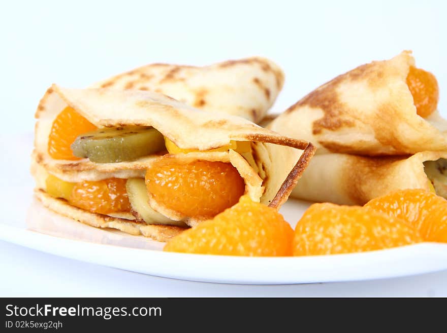 Pancakes stuffed with fruit (peach, kiwi, mandarin) on a plate decorated with fruit