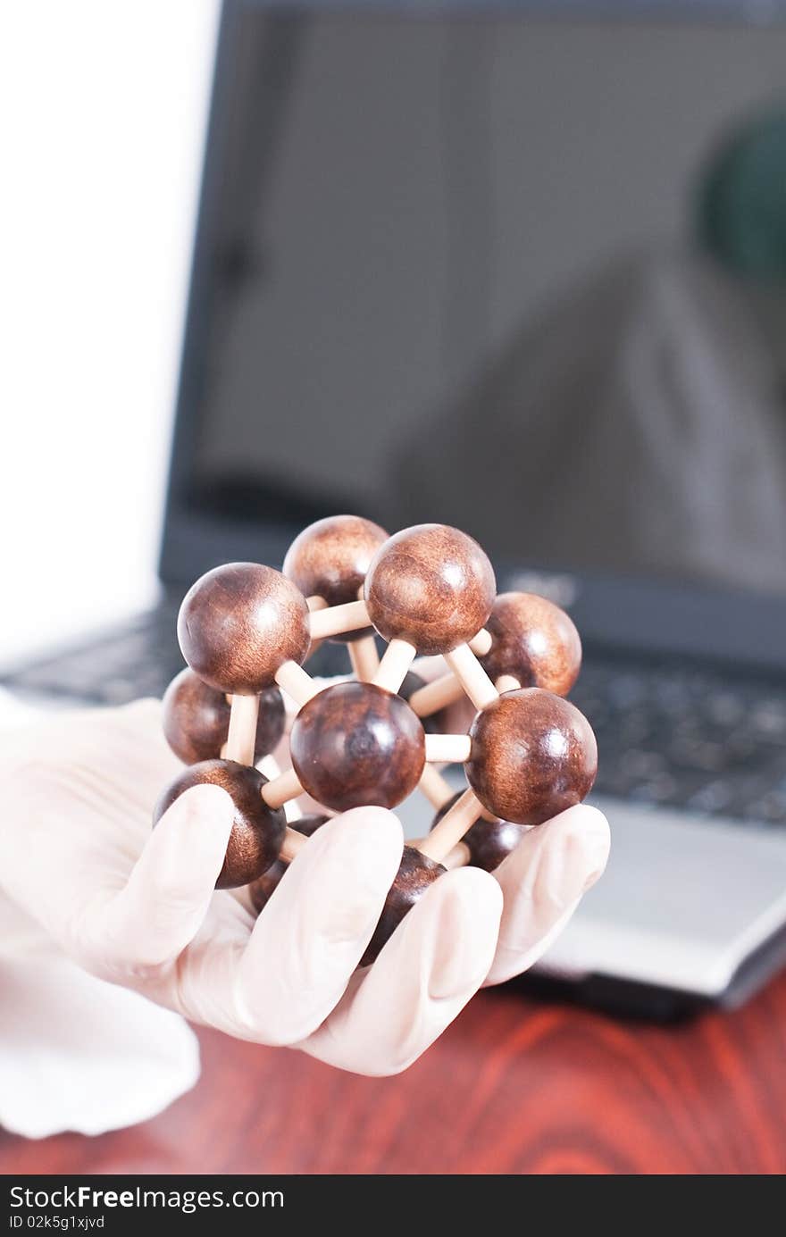 Holding molecule with gloves and laptop in the background