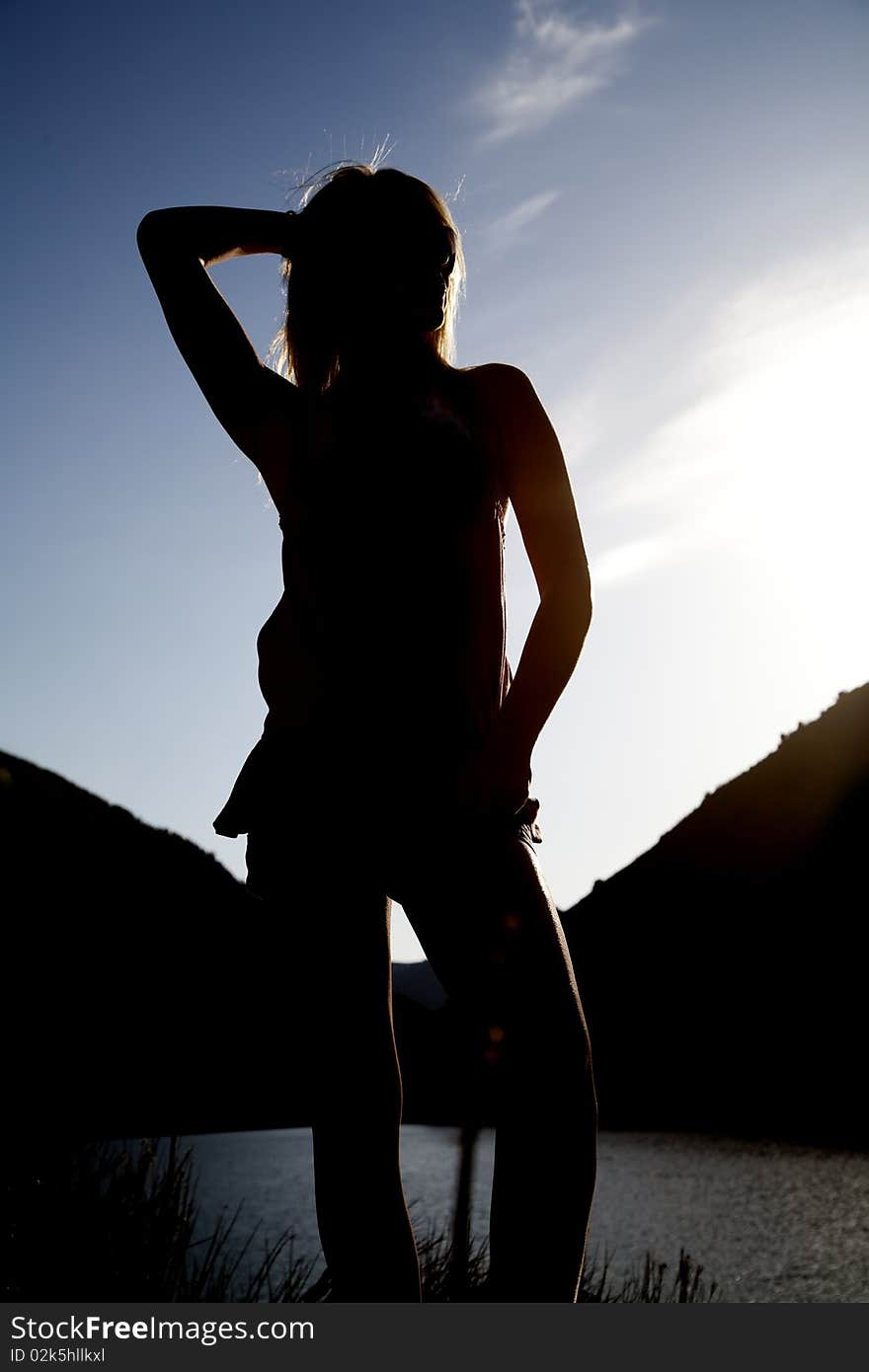 A silhouette of a woman in front of some water with her arm up. A silhouette of a woman in front of some water with her arm up.