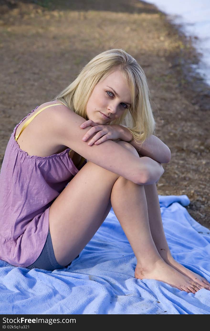 A beautiful woman sitting on a blue blanket on the beach relaxing. A beautiful woman sitting on a blue blanket on the beach relaxing.