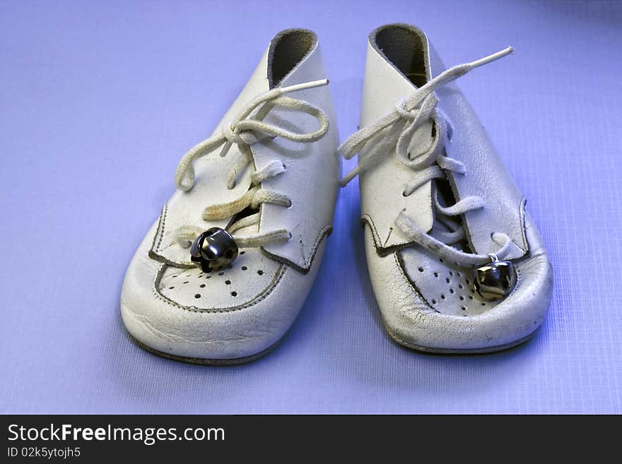 Vintage soft white leather baby shoes on an isolated blue background. Vintage soft white leather baby shoes on an isolated blue background