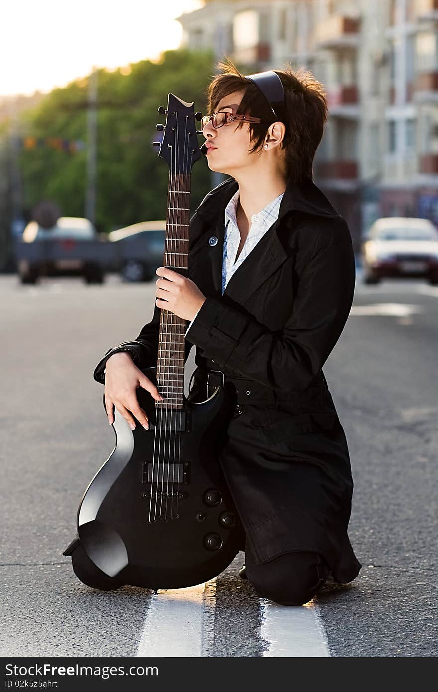 White brunette chick with black electric guitar sitting on the road. White brunette chick with black electric guitar sitting on the road