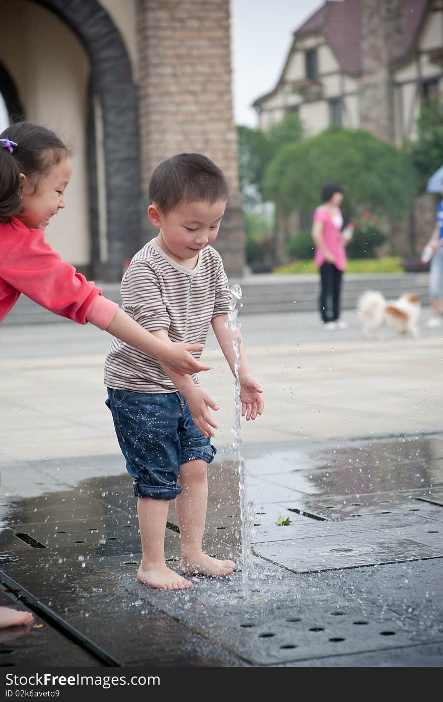 Asian boy and girl play by fountain