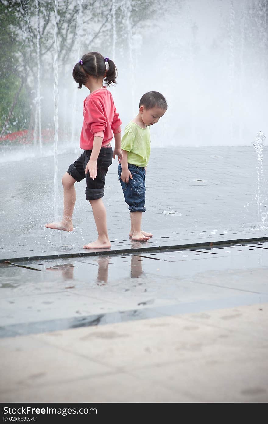 Asian boy and girl play by fountain