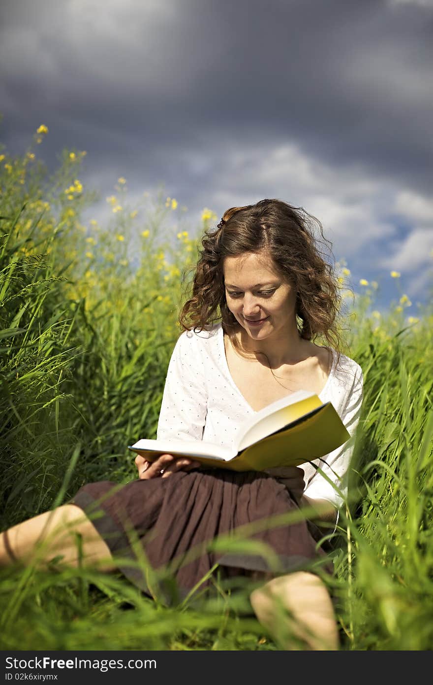 Young smiling woman sitting in green field and reading a book. Young smiling woman sitting in green field and reading a book.