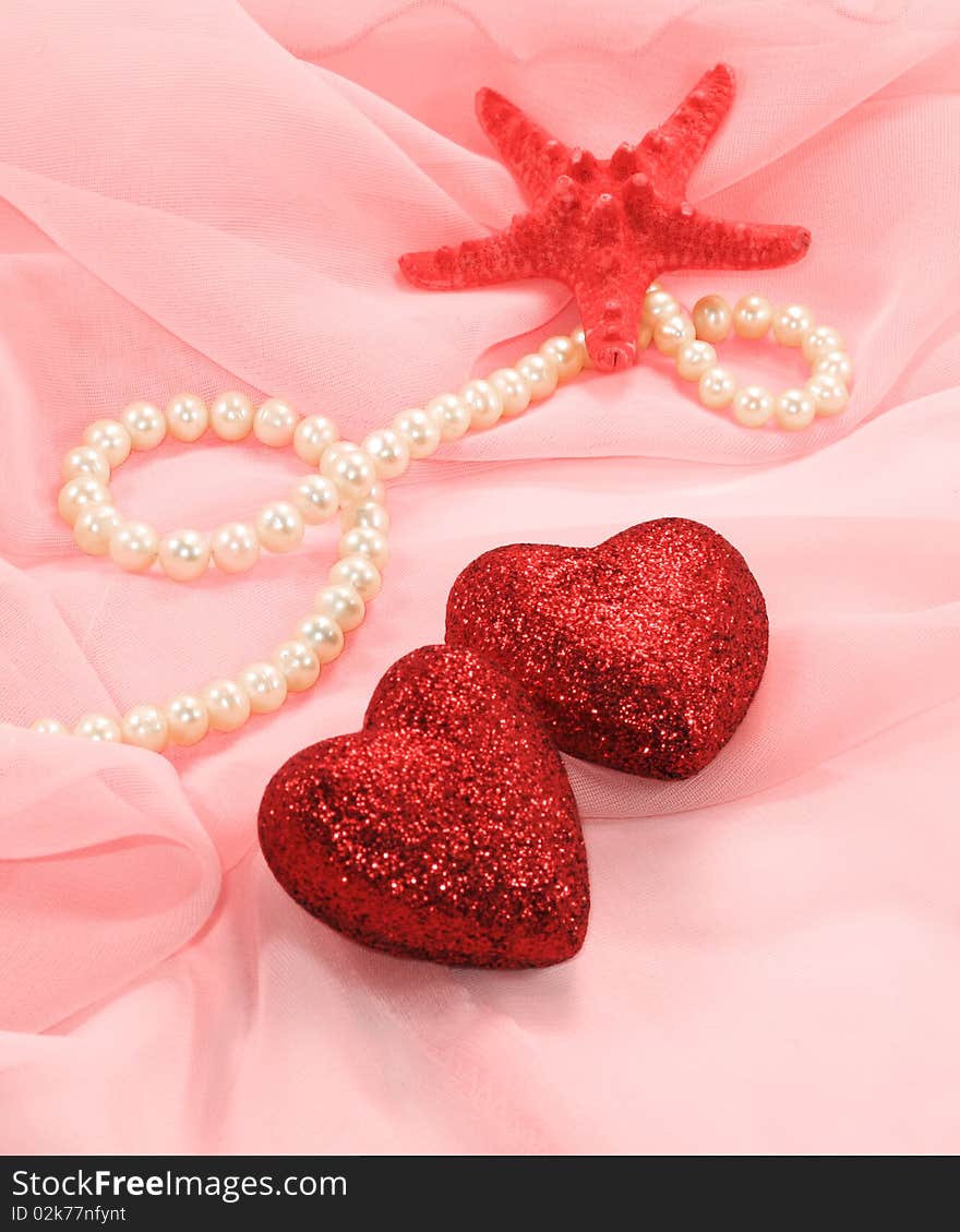 Two sparkling heart, starfish and pearls are on a pink silk. Two sparkling heart, starfish and pearls are on a pink silk