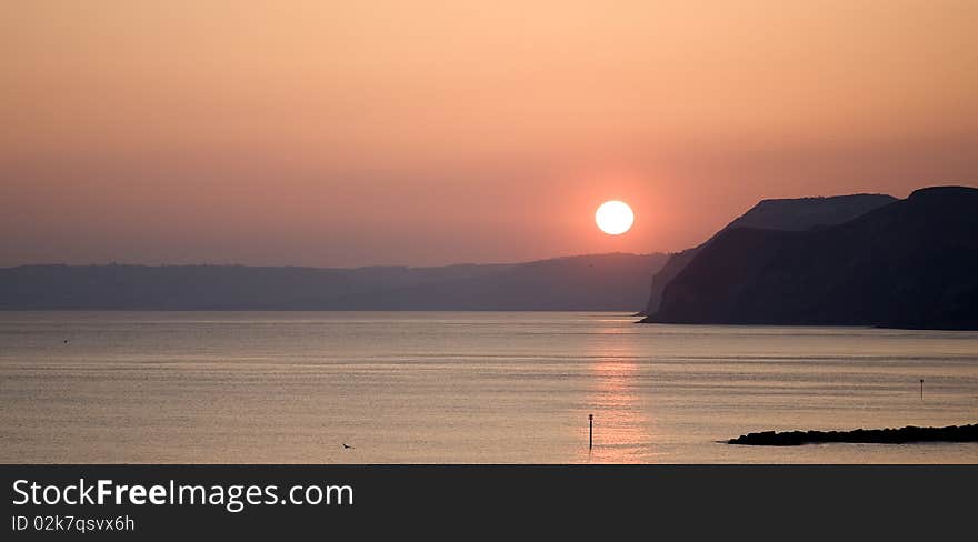 Panoramic shot of setting sun with reflections in ocean and cliffs in middle distance. Panoramic shot of setting sun with reflections in ocean and cliffs in middle distance.