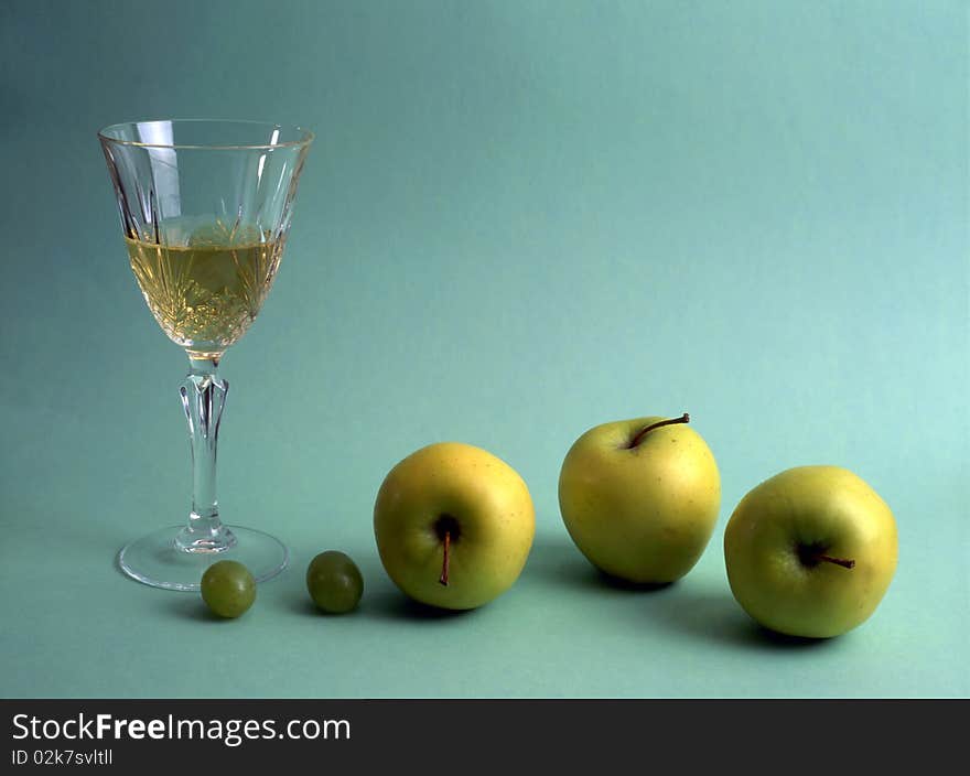 A glass of white wine with fruits isolated on green background. A glass of white wine with fruits isolated on green background