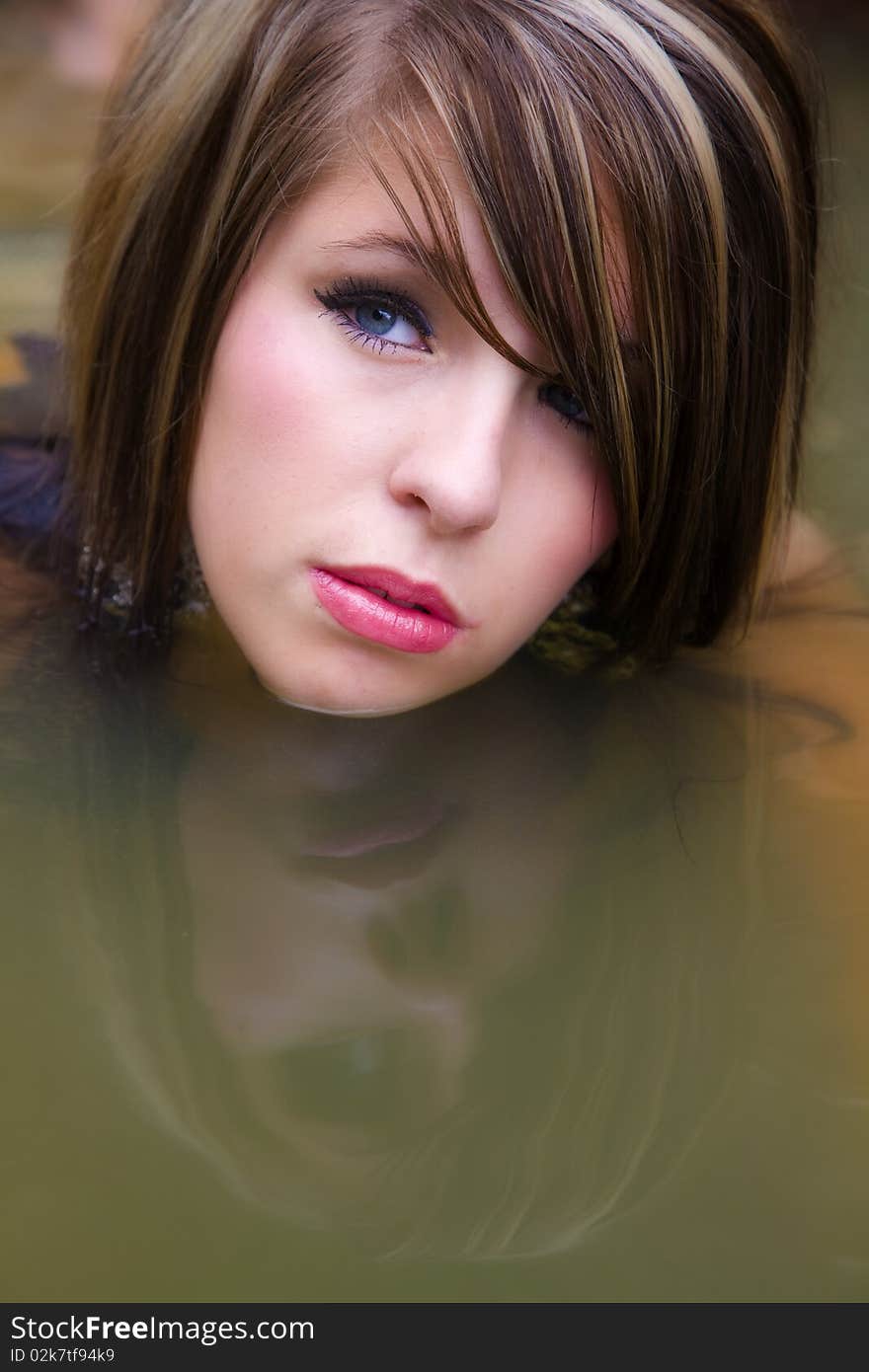 A woman in water with her head reflecting in the water while she has a look as if reflecting on her past. A woman in water with her head reflecting in the water while she has a look as if reflecting on her past.