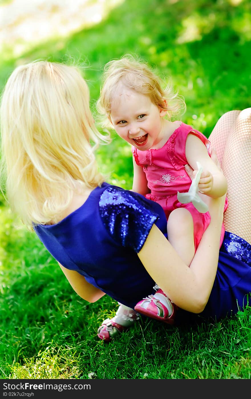 Girl sits on her mother s knees on a green lawn