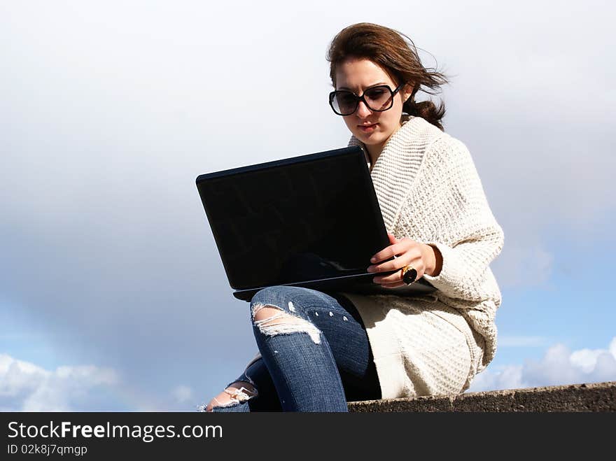 Young woman working with laptop on the beach . Wearing sunglasses and cotton coat . Windy day . Young woman working with laptop on the beach . Wearing sunglasses and cotton coat . Windy day .