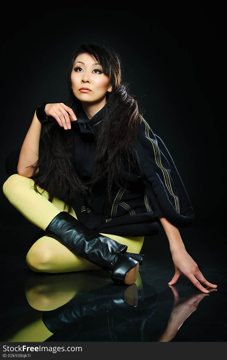 Sitting brunette asian model on black background with night reflections