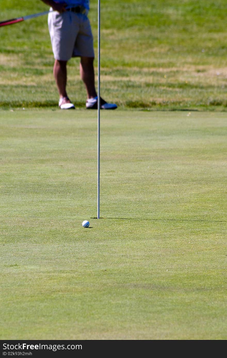 A golf ball on the green while another golfer watches.