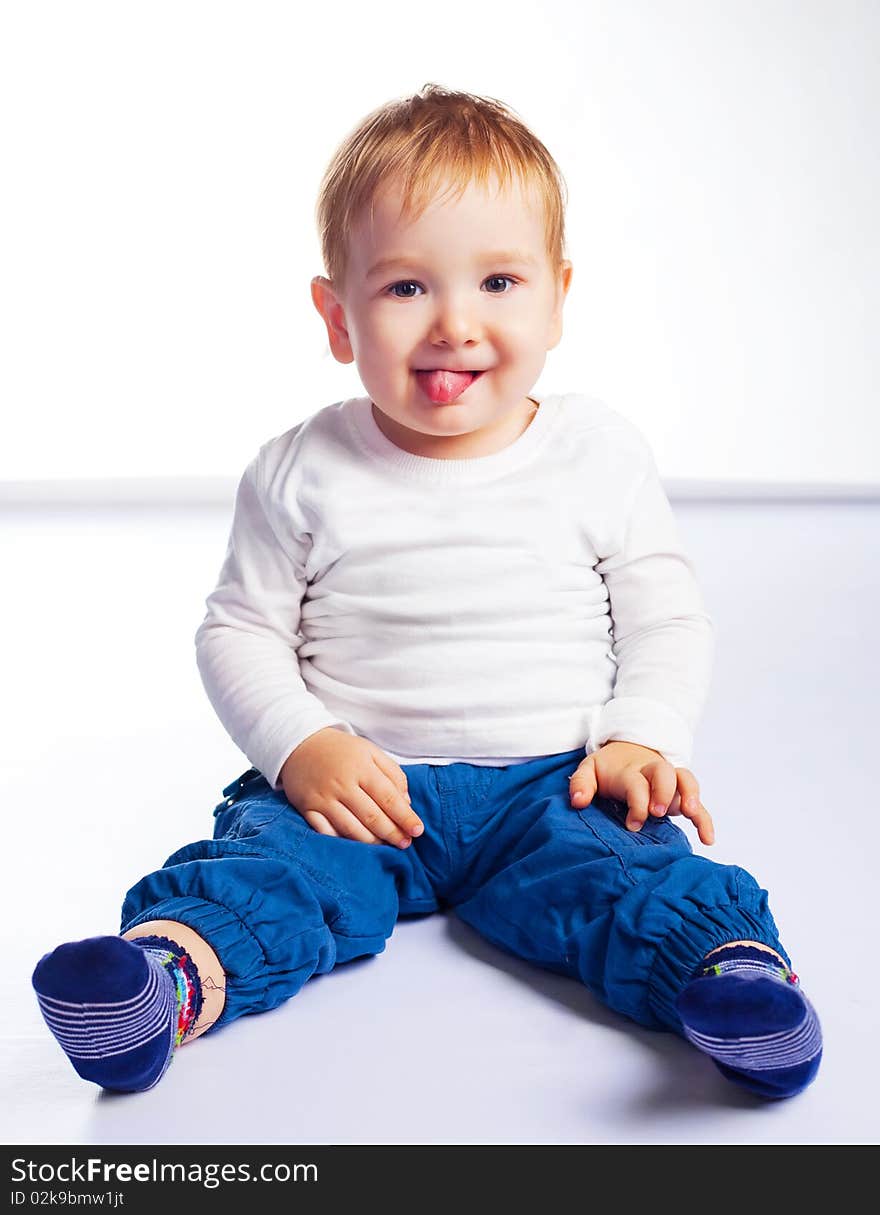 Cute happy baby sitting on the floor and showing tongue