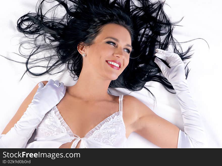 Portrait of a young and happy brunette lying on a silk bed. Image siolated on a white background.