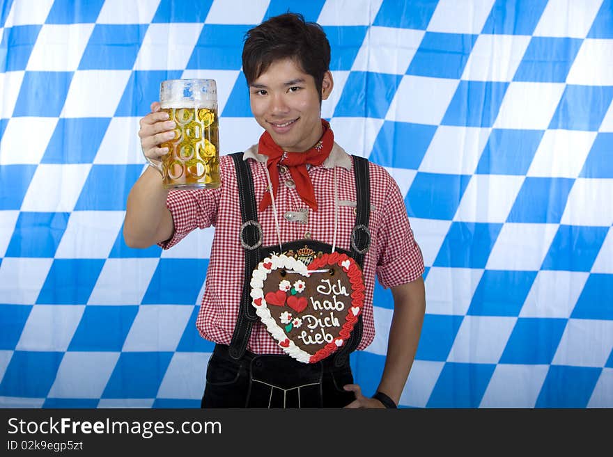 Young man dressed in leather pants (lederhose) holding an Oktoberfest beer stein into camera. In Background is the Bavarian flag visible. Young man dressed in leather pants (lederhose) holding an Oktoberfest beer stein into camera. In Background is the Bavarian flag visible.