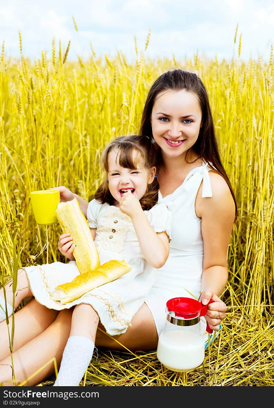 Happy mother and her little daughter having a picnic in the wheat field