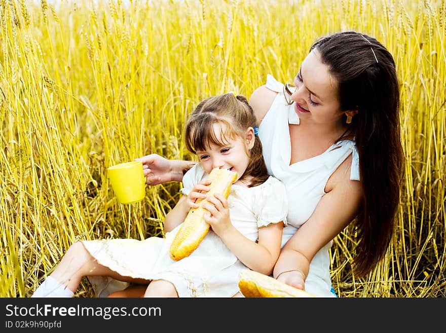 Happy mother and her  little daughter having a picnic  in the wheat field