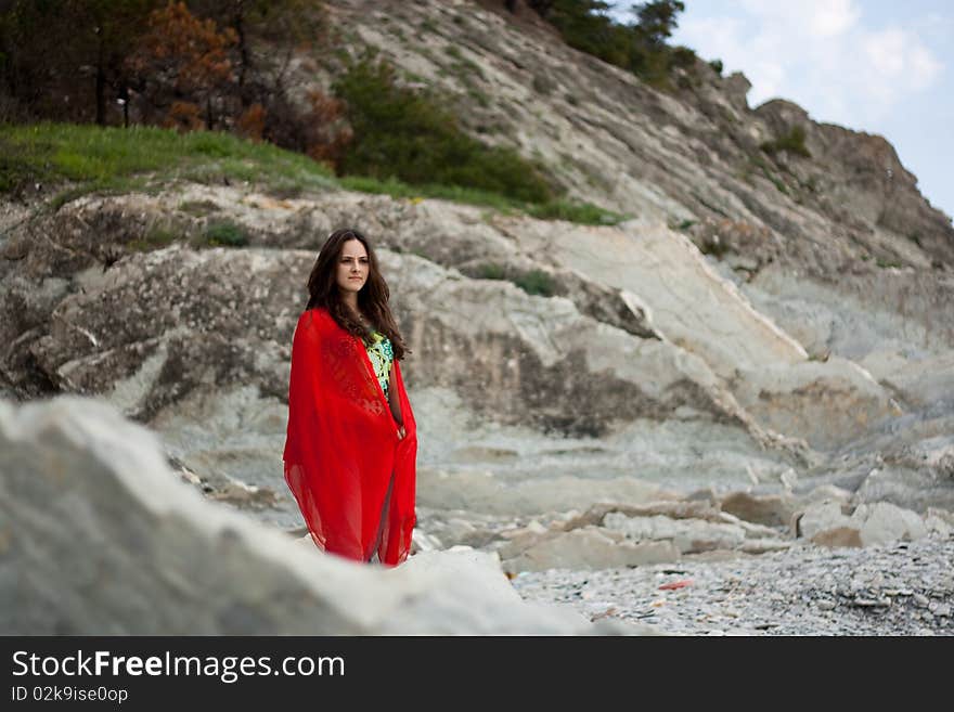 A girl in a red pillow-sham stands ashore and waits someone. A girl in a red pillow-sham stands ashore and waits someone