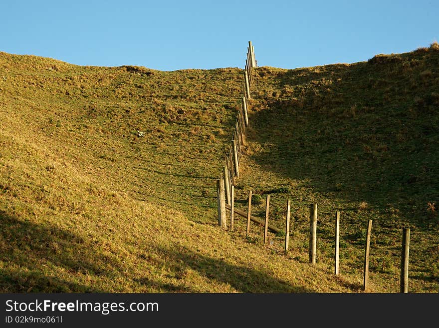 Fence running uphill, disecting fields under blue sky. Fence running uphill, disecting fields under blue sky.