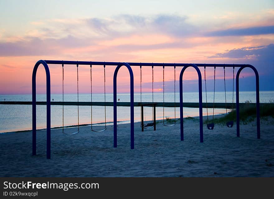 The swing set on the beach in Frankfort, Michigan is silhouetted against the sunset. The swing set on the beach in Frankfort, Michigan is silhouetted against the sunset.