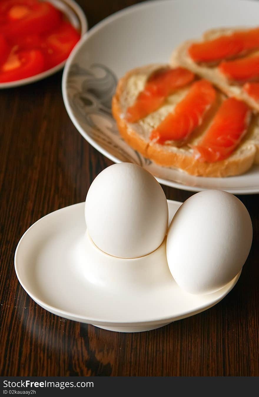 Close-up healthy breakfast - two boiled eggs, sliced tomatoes and sandwiches with salty salmon