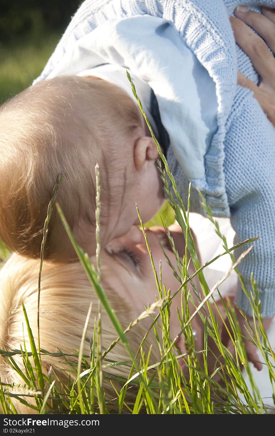 Young happy mother with a child lying embraced on the green grass in the park