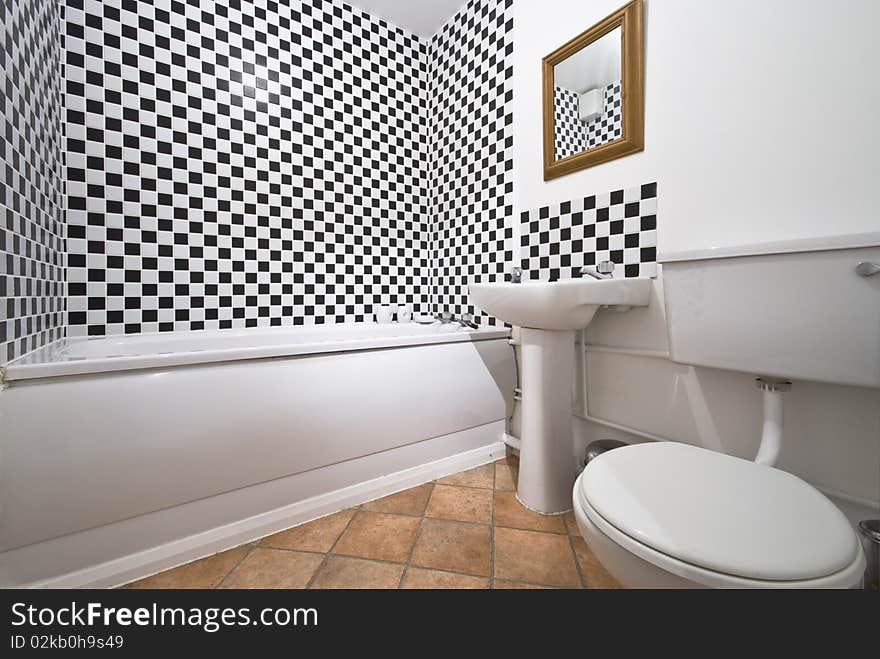 Classy bathroom with large bath tub, white ceramic wash basin and toilet with black and white chessboard pattern tiles. Classy bathroom with large bath tub, white ceramic wash basin and toilet with black and white chessboard pattern tiles