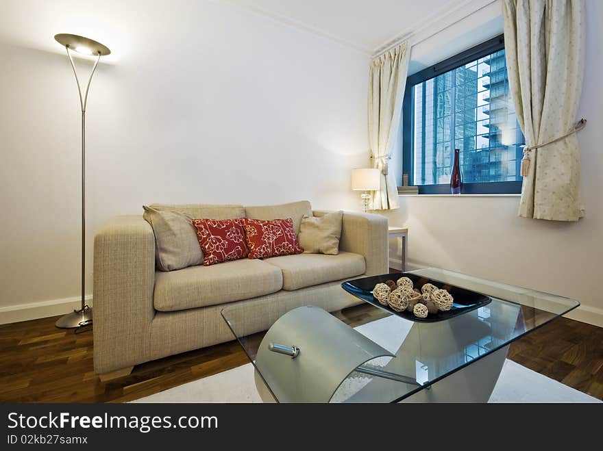 Modern living room with beige sofa with decorative cushions and glass top designer coffee table