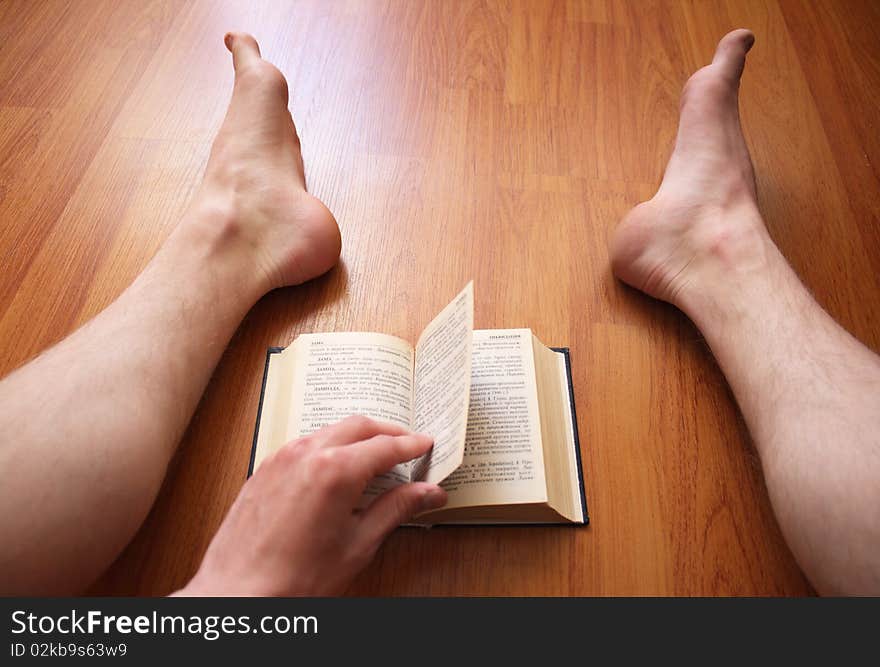 The person sits on a floor and reads the book. The person sits on a floor and reads the book