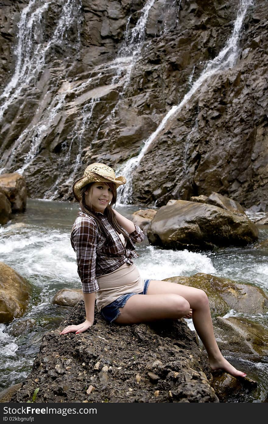 A beautiful woman dressed like a cowgirl on a rock by the river. A beautiful woman dressed like a cowgirl on a rock by the river.