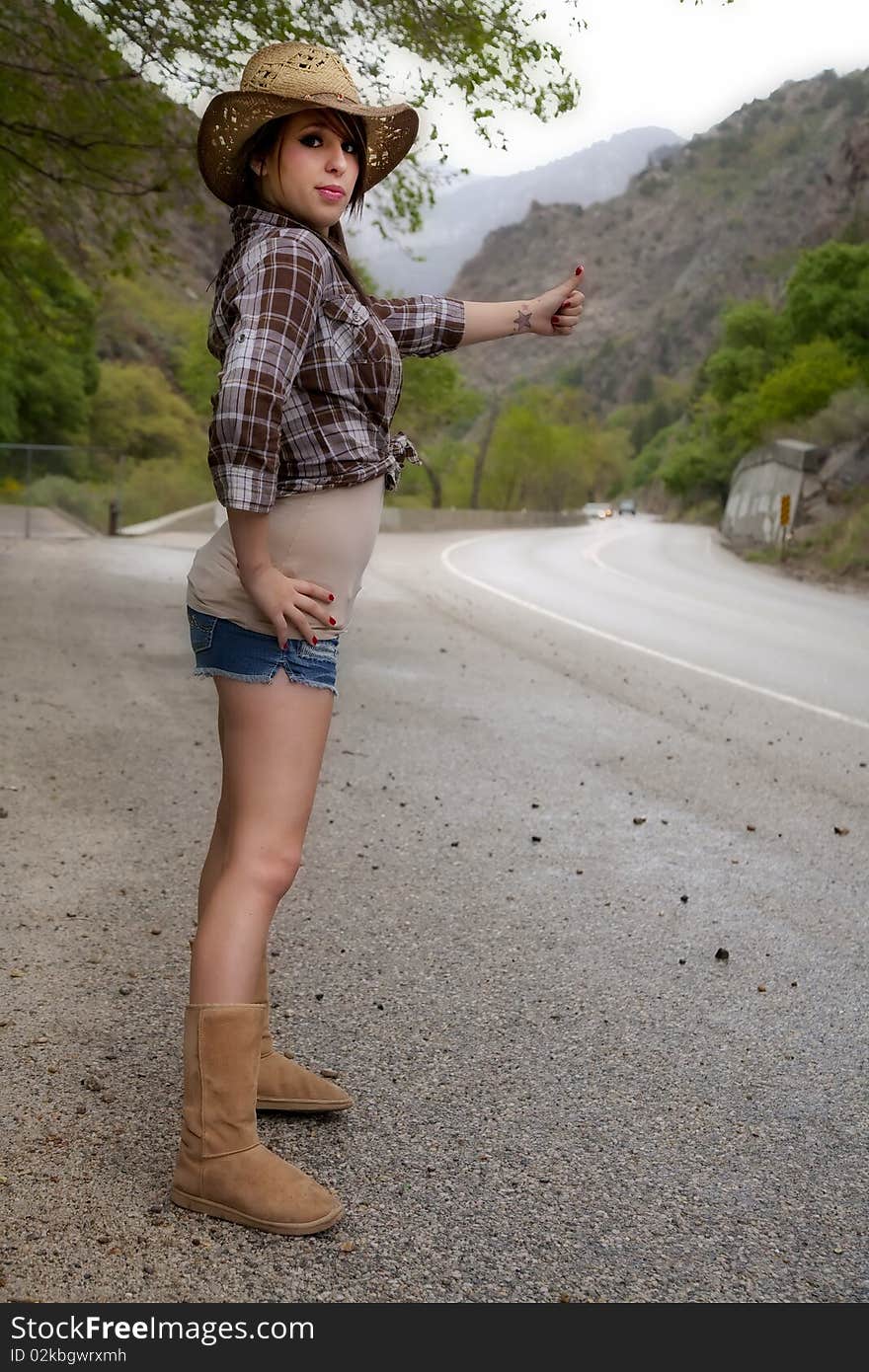 A young country woman is hitch hiking by the highway. A young country woman is hitch hiking by the highway.