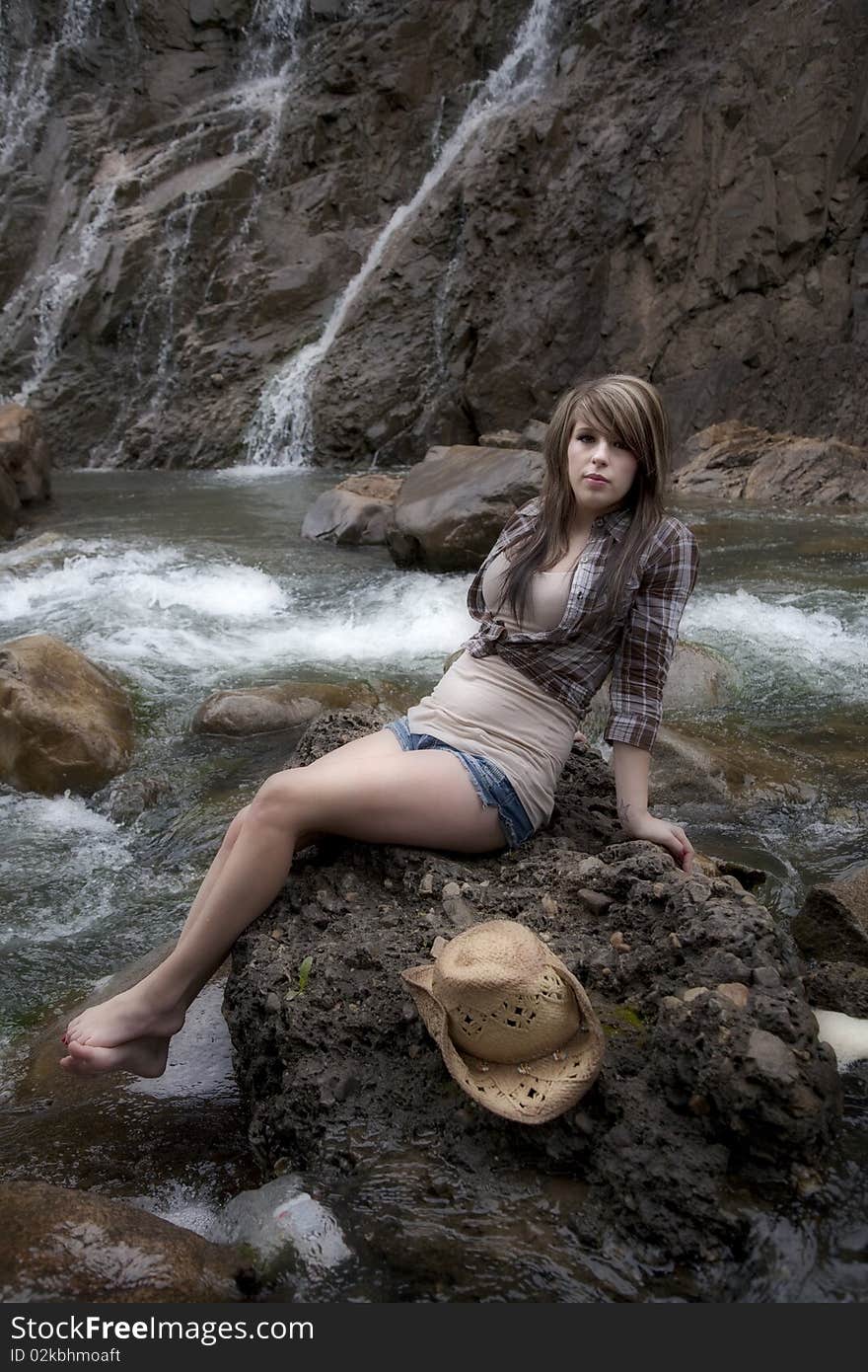 A beautiful woman dressed like a cowgirl on a rock by the river. A beautiful woman dressed like a cowgirl on a rock by the river.