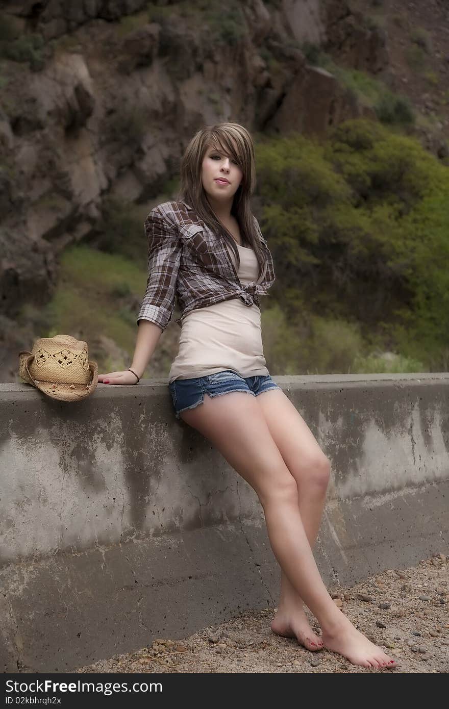 A woman is sitting against a wall with her hat by her. A woman is sitting against a wall with her hat by her.