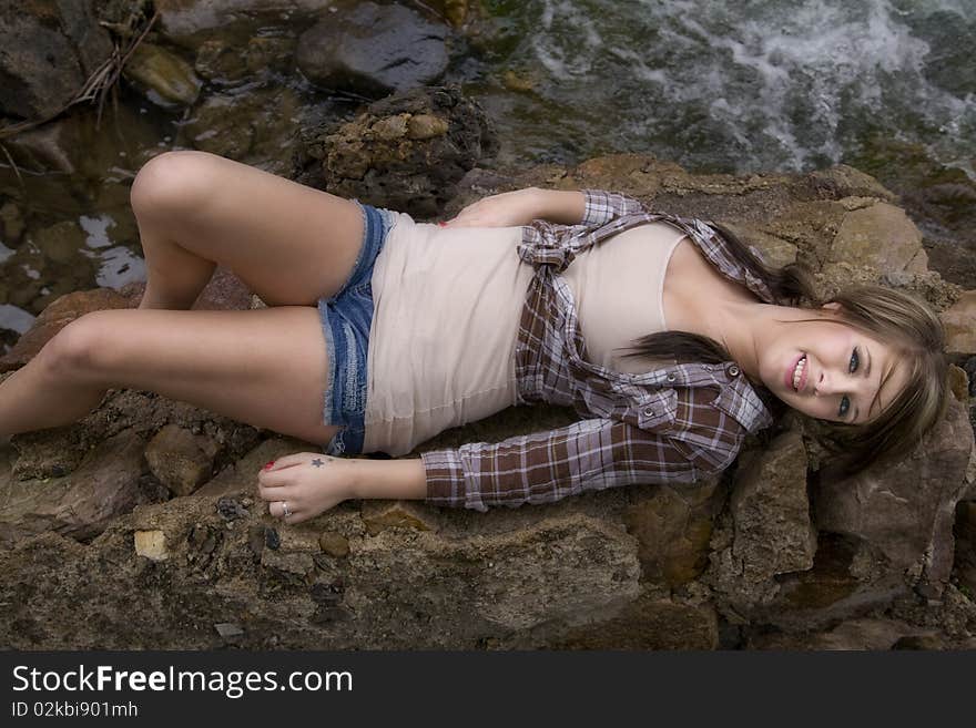 A woman is laying on her back on a big rock with the river right by her. A woman is laying on her back on a big rock with the river right by her.