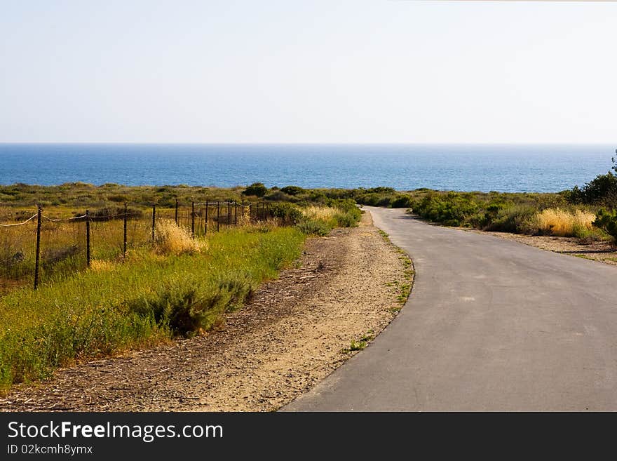 A one-lane country road leads through a field down toward the beach. A one-lane country road leads through a field down toward the beach.