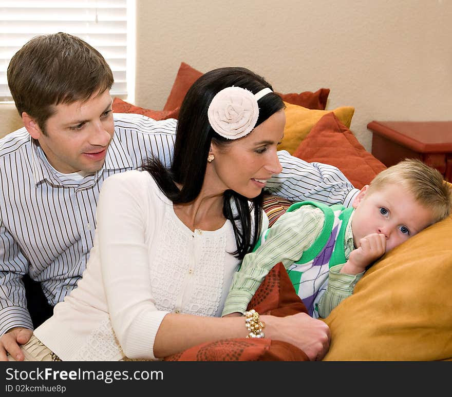 A family at home, with the father and mother looking tenderly at their young son as they sit amidst colorful cushions on their couch. A family at home, with the father and mother looking tenderly at their young son as they sit amidst colorful cushions on their couch.