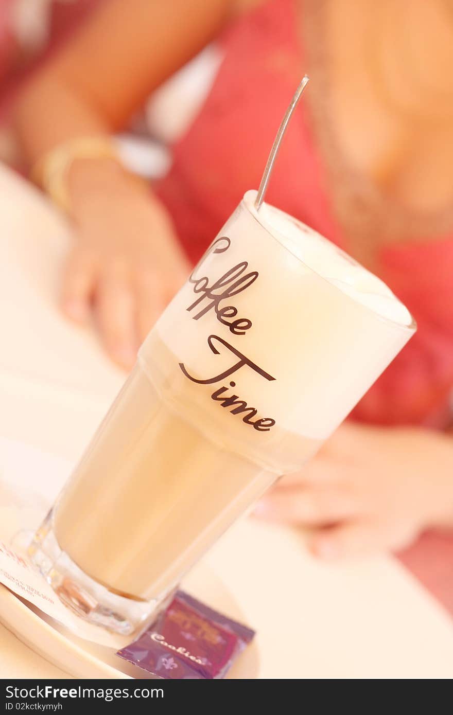 A glass with lettering coffee time a spoon and a cookie on a table